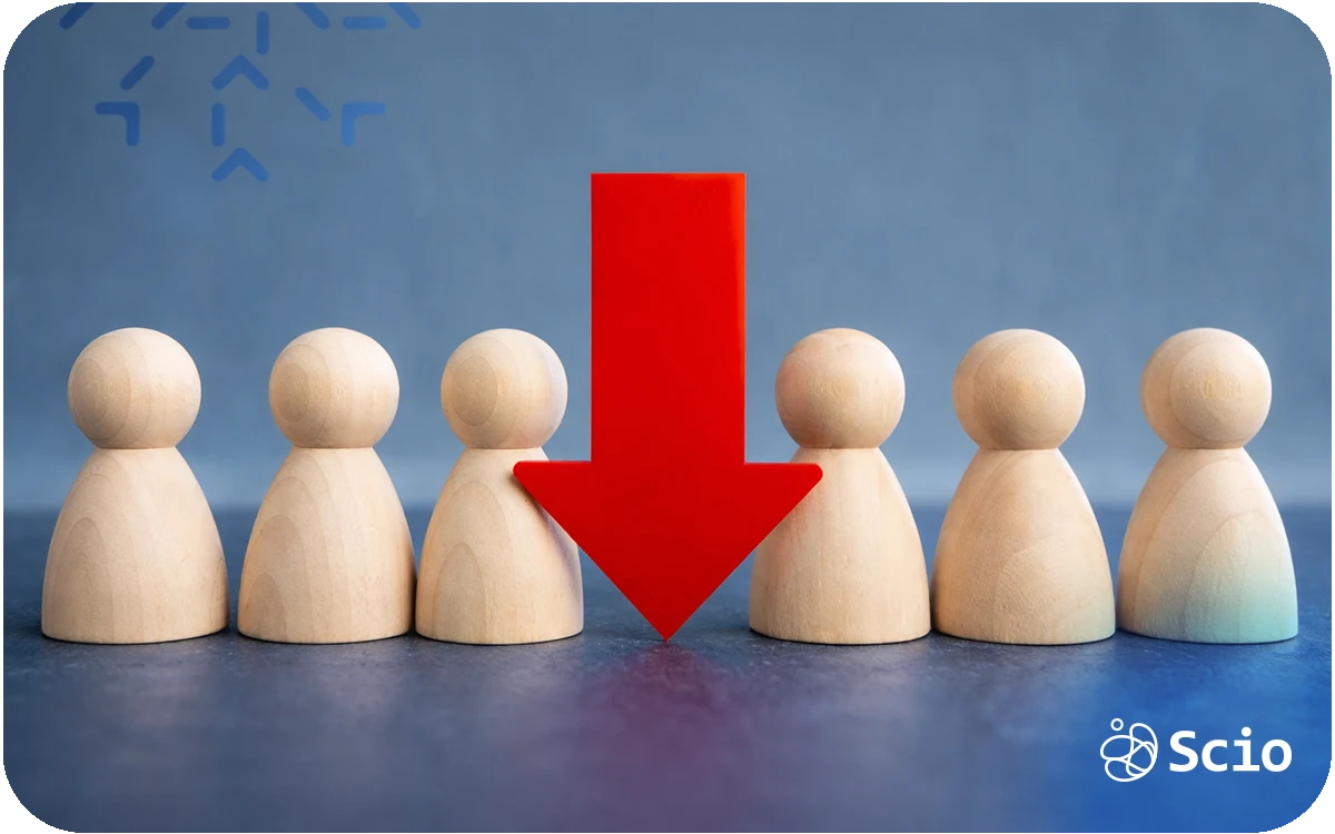 Wooden figures in a row with a red arrow pointing down at one, symbolizing team dependency risk and the Bus Factor concept.