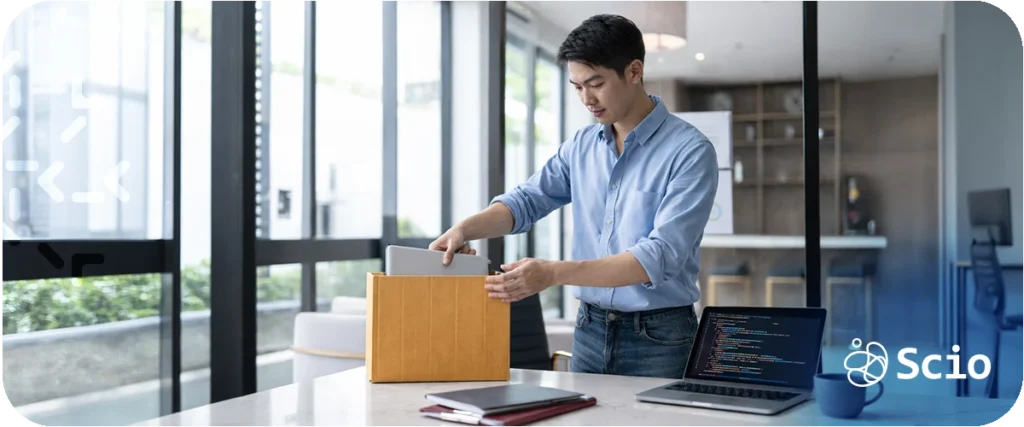 Software engineer leaving the office with a box during the Great Resignation, laptop with code open on desk.