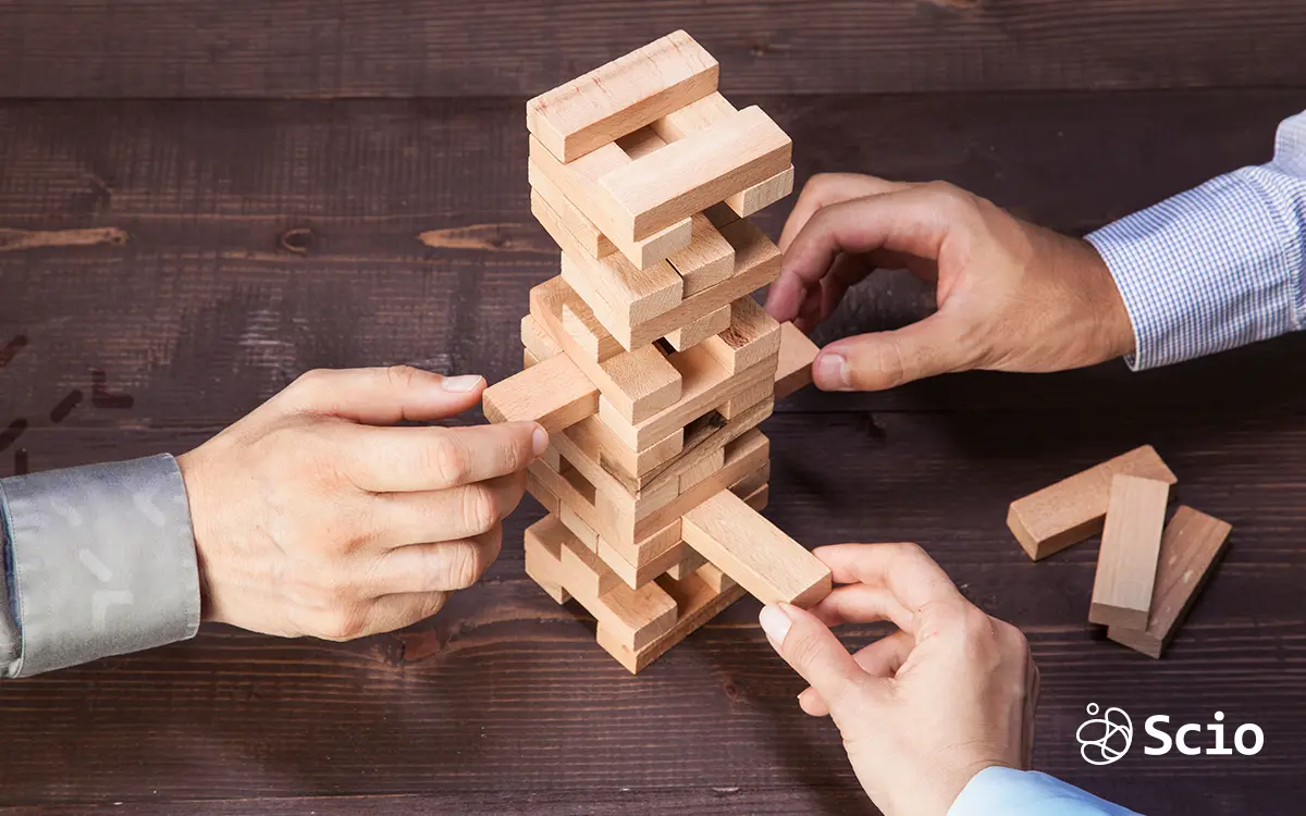 Business hands playing Jenga on a wooden table, representing the balance of risks and strategy in choosing a nearshore or offshore software partner.