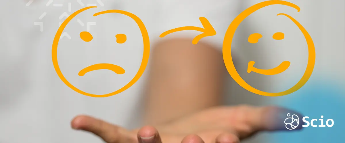 A hand holding a transition from a sad face to a happy face, symbolizing emotional recovery from burnout in dev teams.