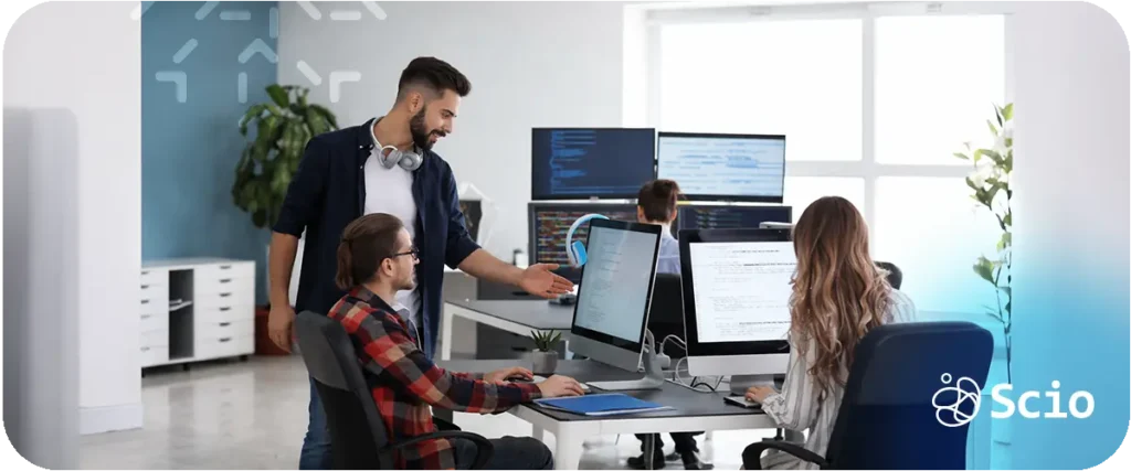 Software engineering team collaborating around multiple monitors while reviewing code and coordinating development tasks.