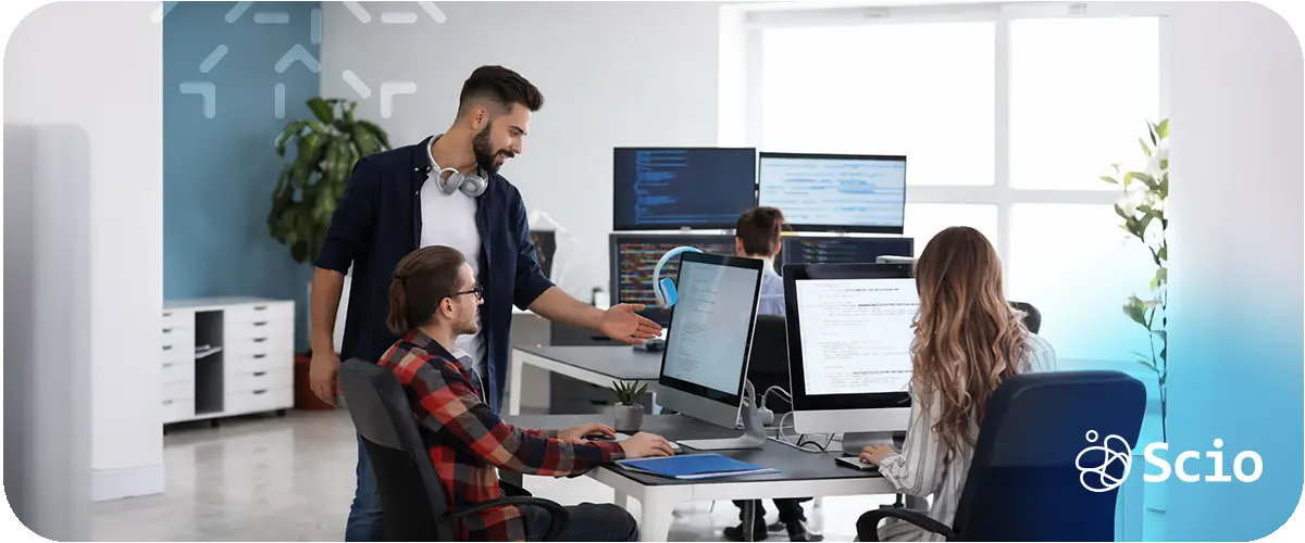 Software engineering team collaborating around multiple monitors while reviewing code and coordinating development tasks